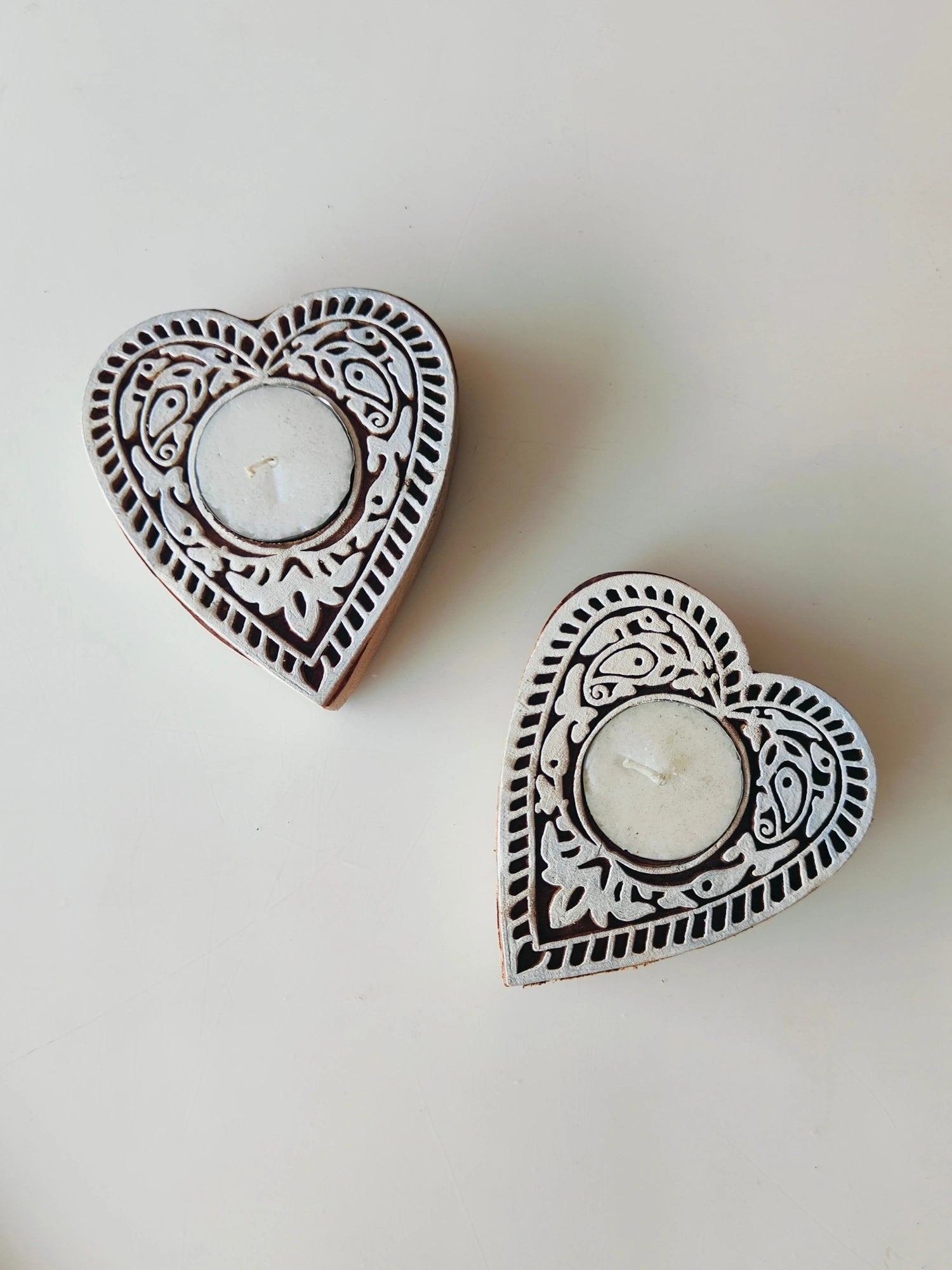 Two heart-shaped wooden tea light holders with intricate carvings and a natural wood finish, each holding a tea light candle.