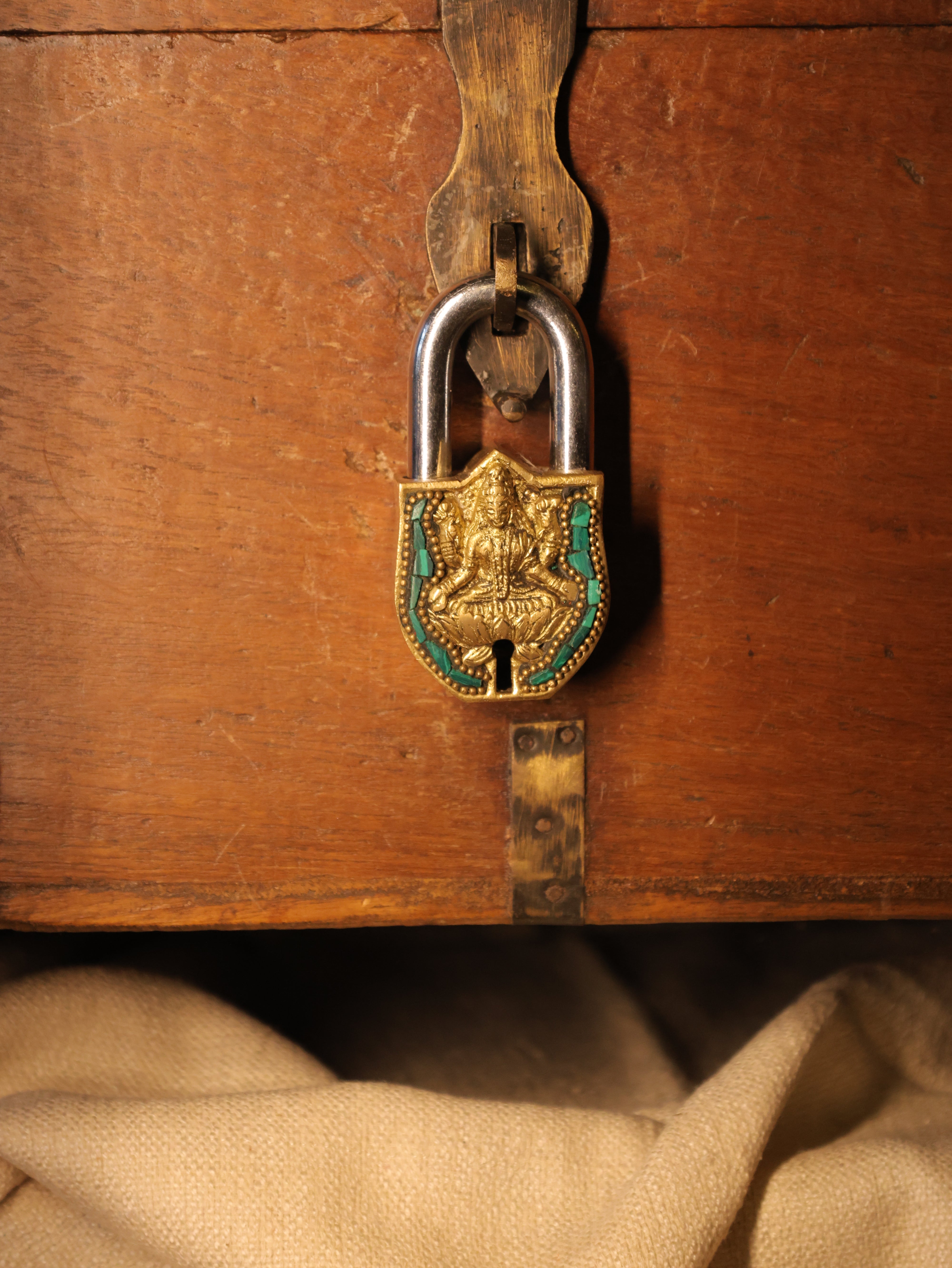 Close-up of a wooden chest with a decorative lock featuring gold, green, and silver elements.