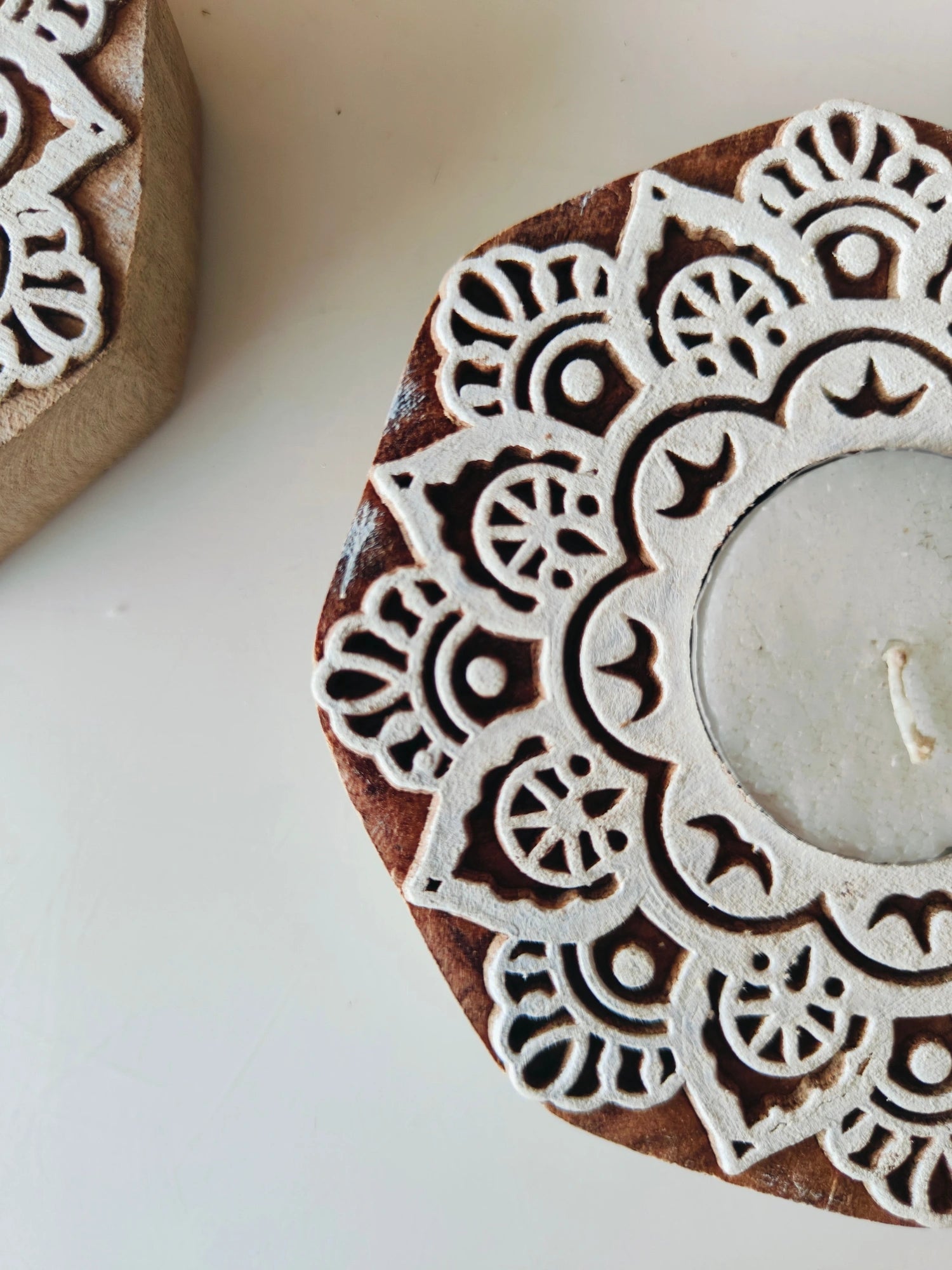 A handmade wooden block tealight holder with a round shape and a white mandala-style pattern, containing a lit tealight candle.