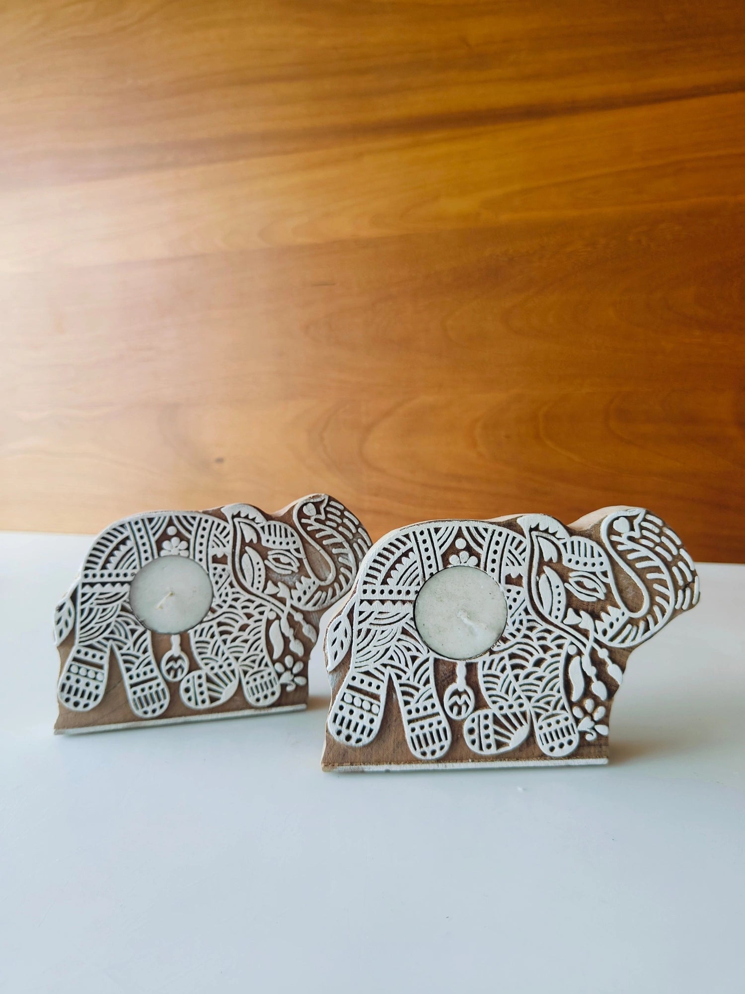 Two handmade wooden elephant-shaped candle holders with intricate patterns, designed to hold tea light candles.