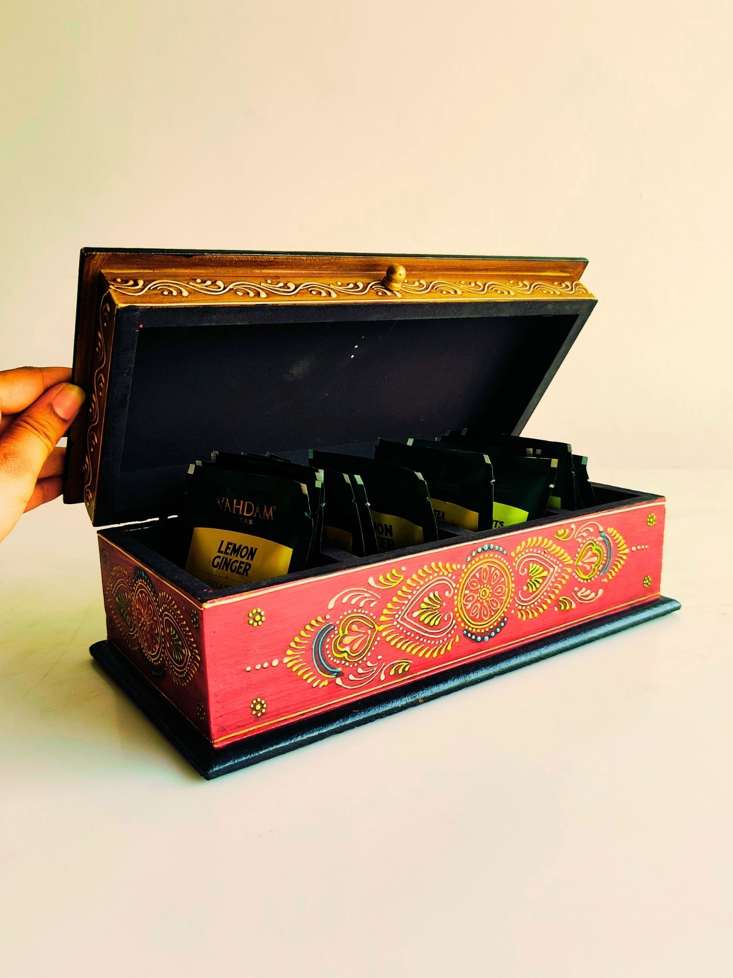 A hand-painted wooden storage box with compartments, featuring vibrant colors and traditional Indian patterns, is open with items arranged inside.
